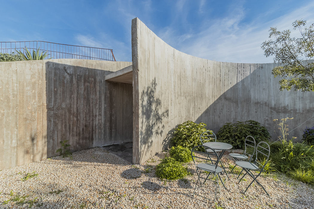 Concrete walls, gravel patio, and minimalist outdoor furniture create a serene space.
