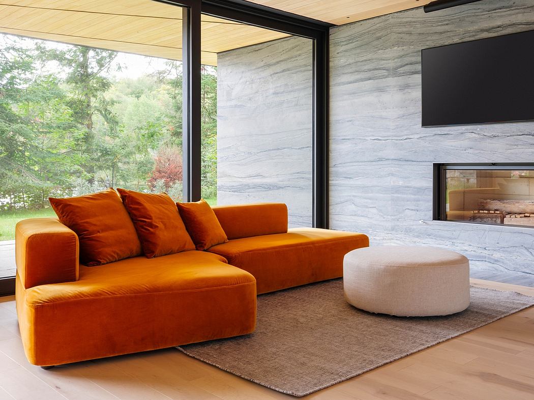 Modern living room with an orange velvet sofa, a white pouf, and large windows overlooking nature.