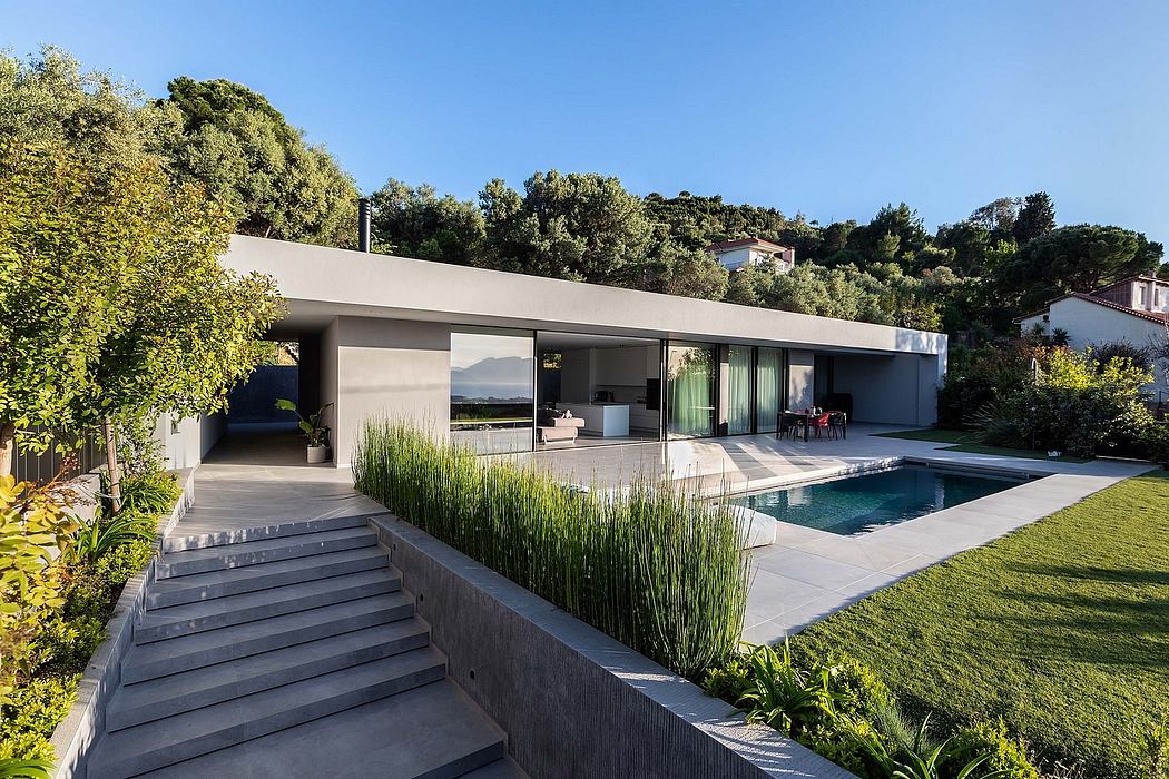 Modern single-story house with sleek design, large windows, and a swimming pool surrounded by lush greenery.