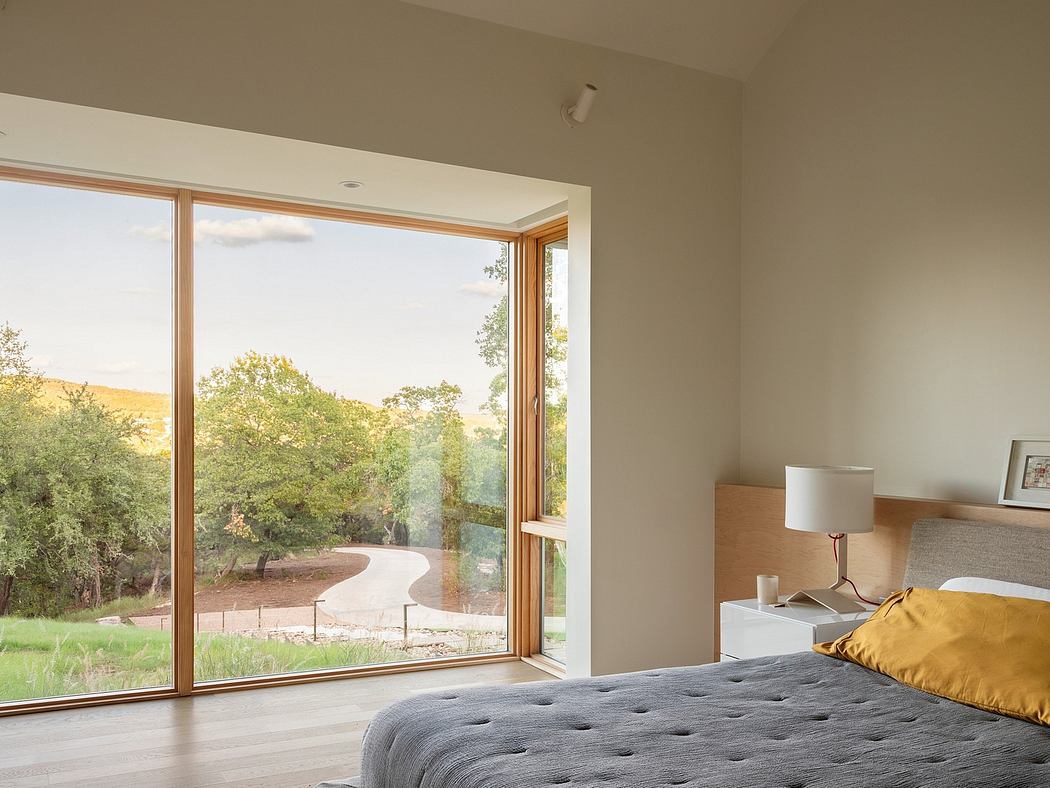 Spacious bedroom with large windows offering scenic woodland view and minimalist decor.