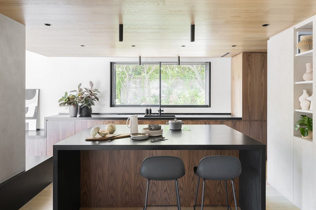 Modern, minimalist kitchen with wooden cabinetry, black countertop, and large window overlooking lush greenery.