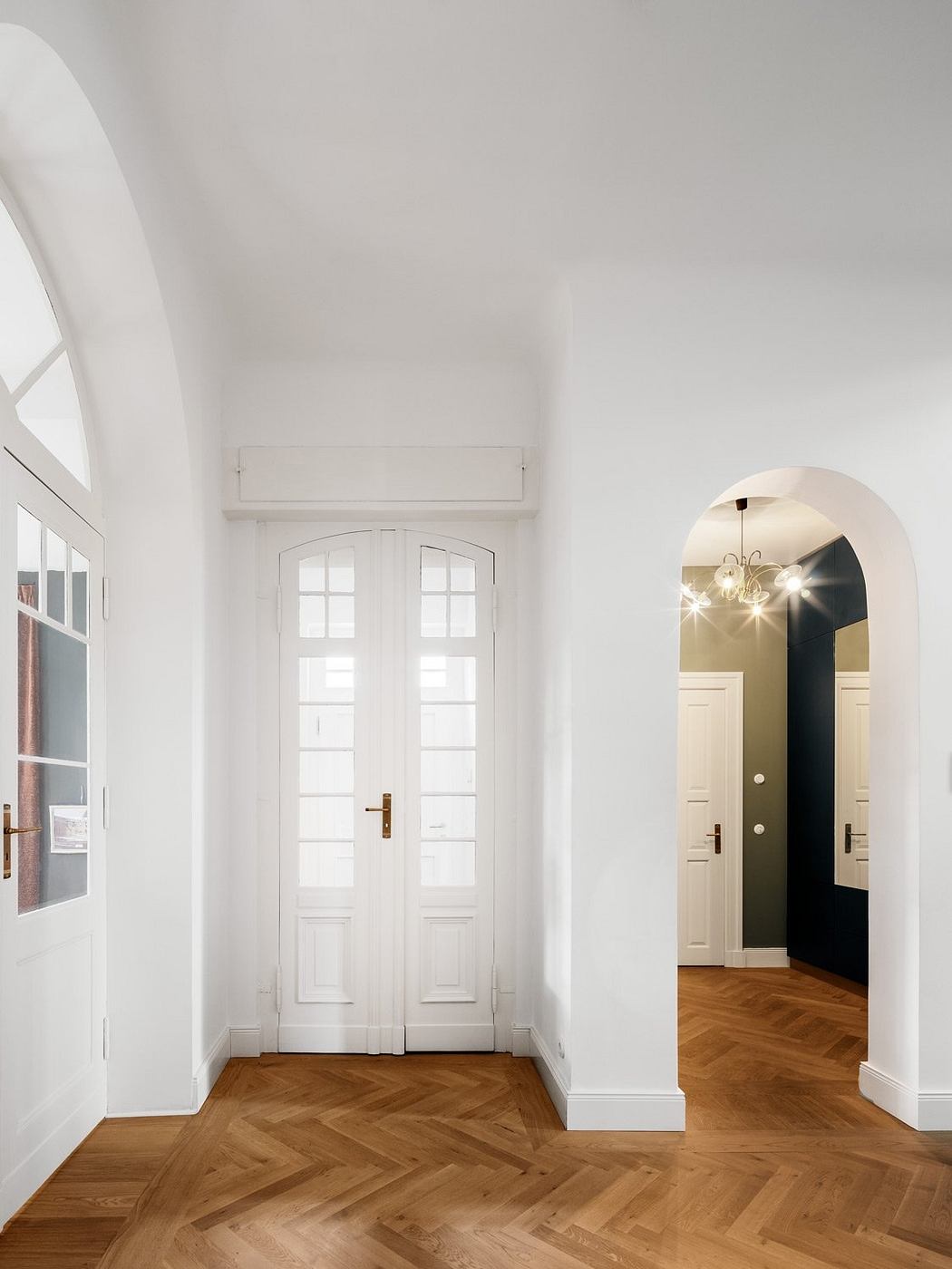 Bright, modern entryway with arched doorways, wooden herringbone floors, and recessed lighting.