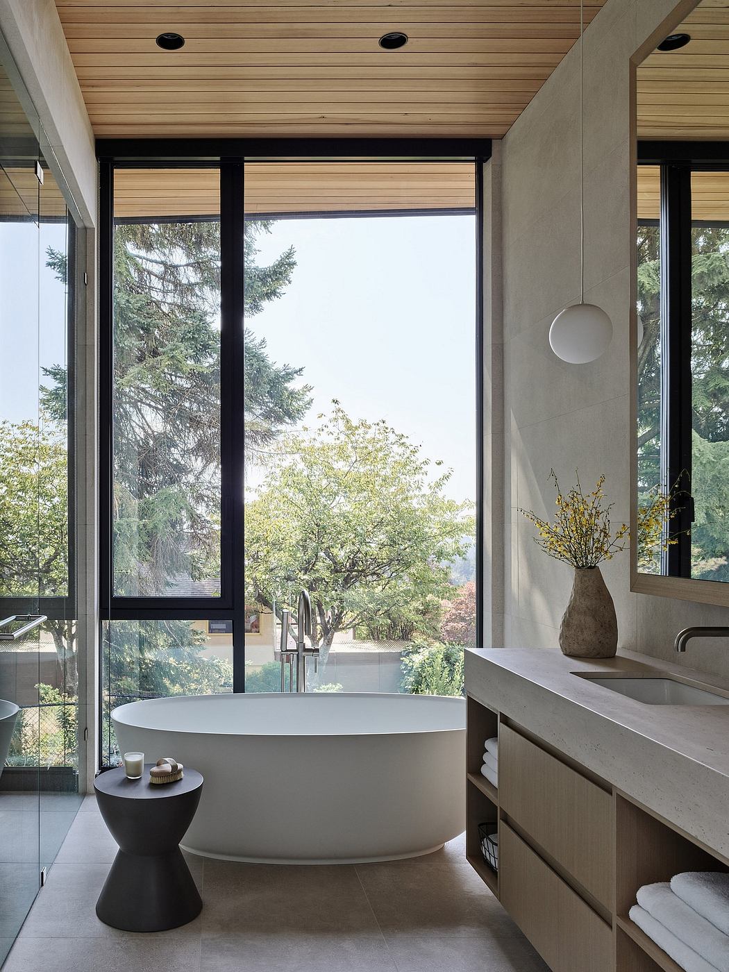 A modern bathroom with a large freestanding tub, sleek wooden vanity, and expansive forest views.