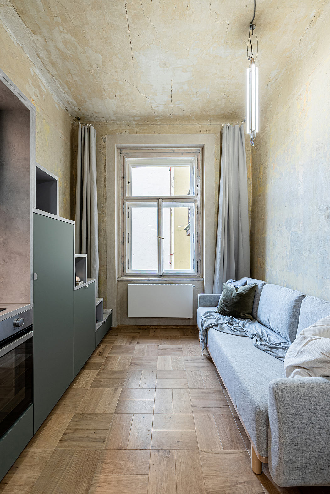 A narrow room with wood-paneled floors, a large window, and a couch against the wall.