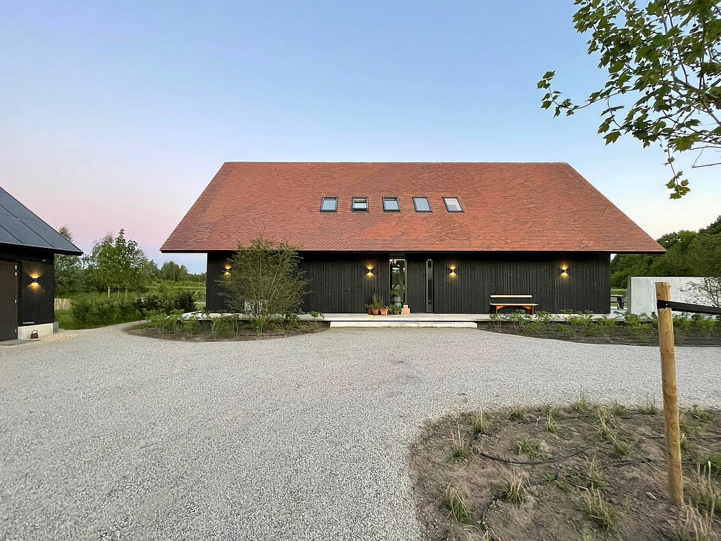 Modern barn-style building with black wooden exterior, large windows, and gravel driveway.