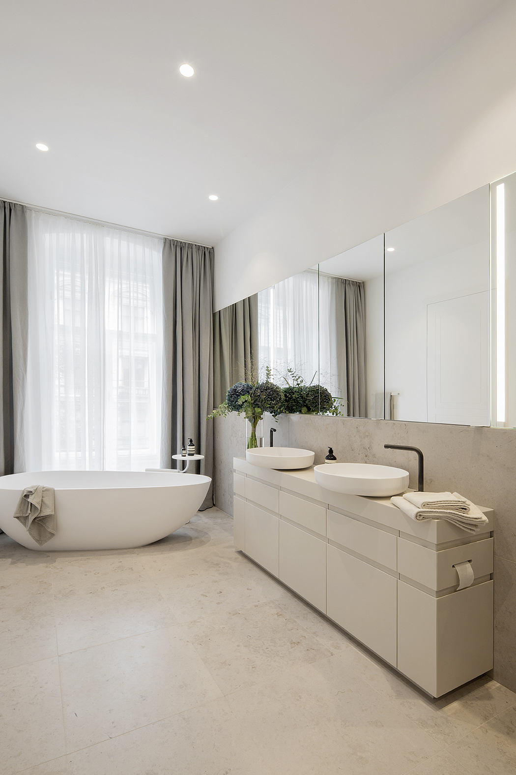 Modern, minimalist bathroom with a freestanding bathtub, dual vanity, and gray curtains.