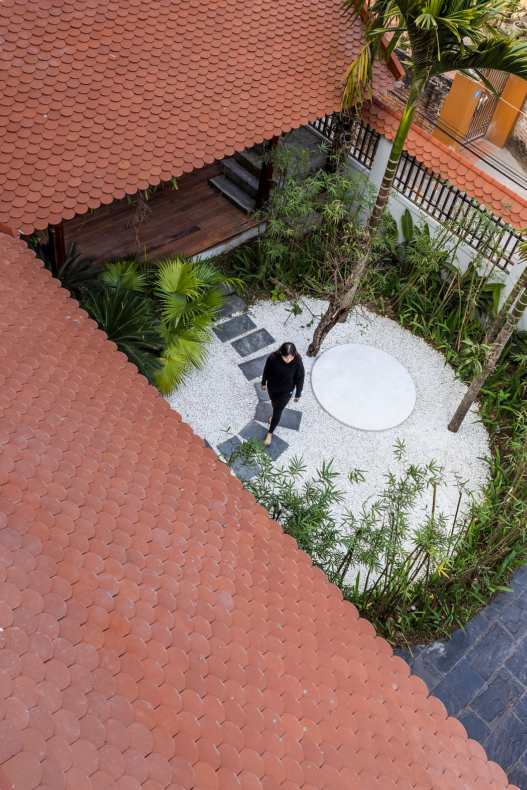 Vibrant terracotta roof tiles, lush greenery, and a minimalist stone patio create a serene oasis.