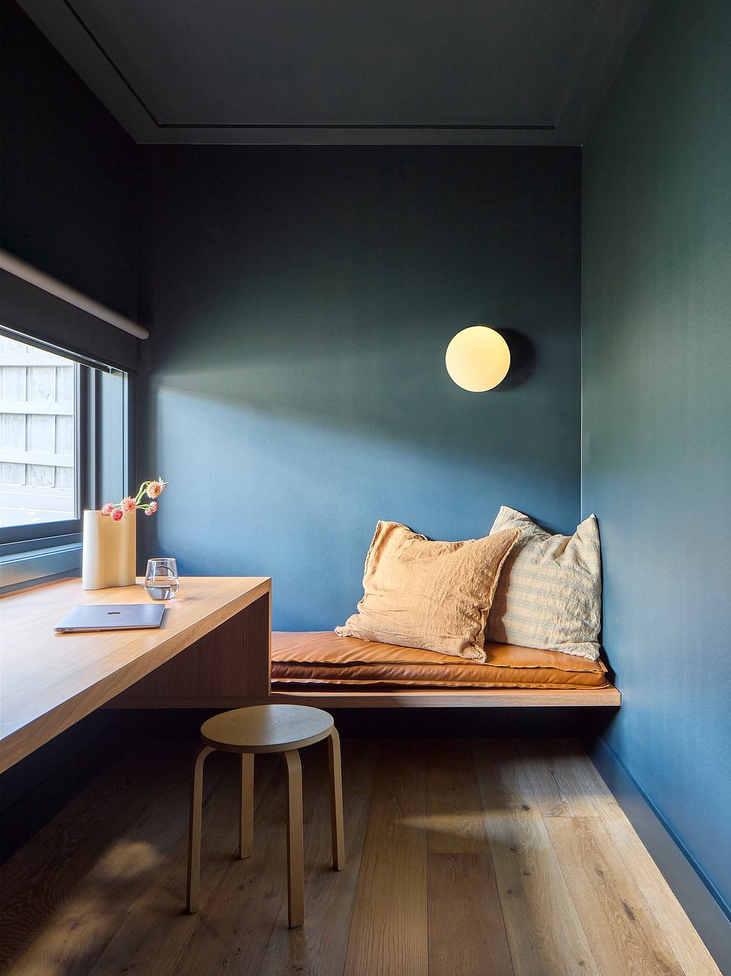 Cozy window nook with wooden bench, pillows, and a minimalist desk and stool.