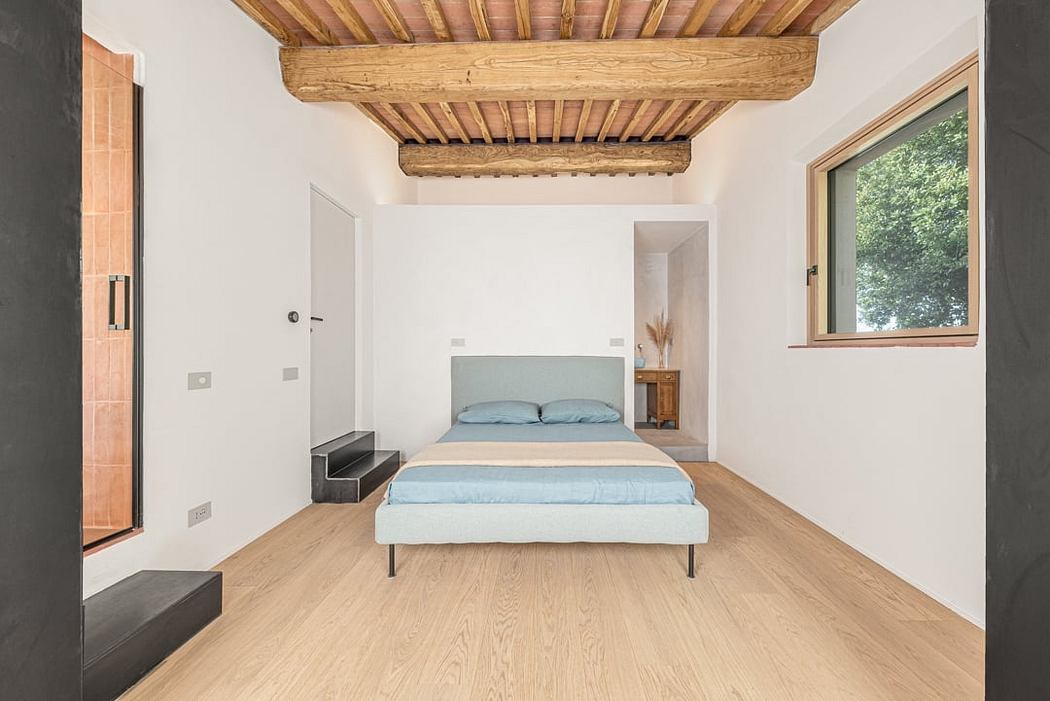 Spacious room with white walls, wooden beamed ceiling, and hardwood flooring. Minimalist bed frame with blue bedding.