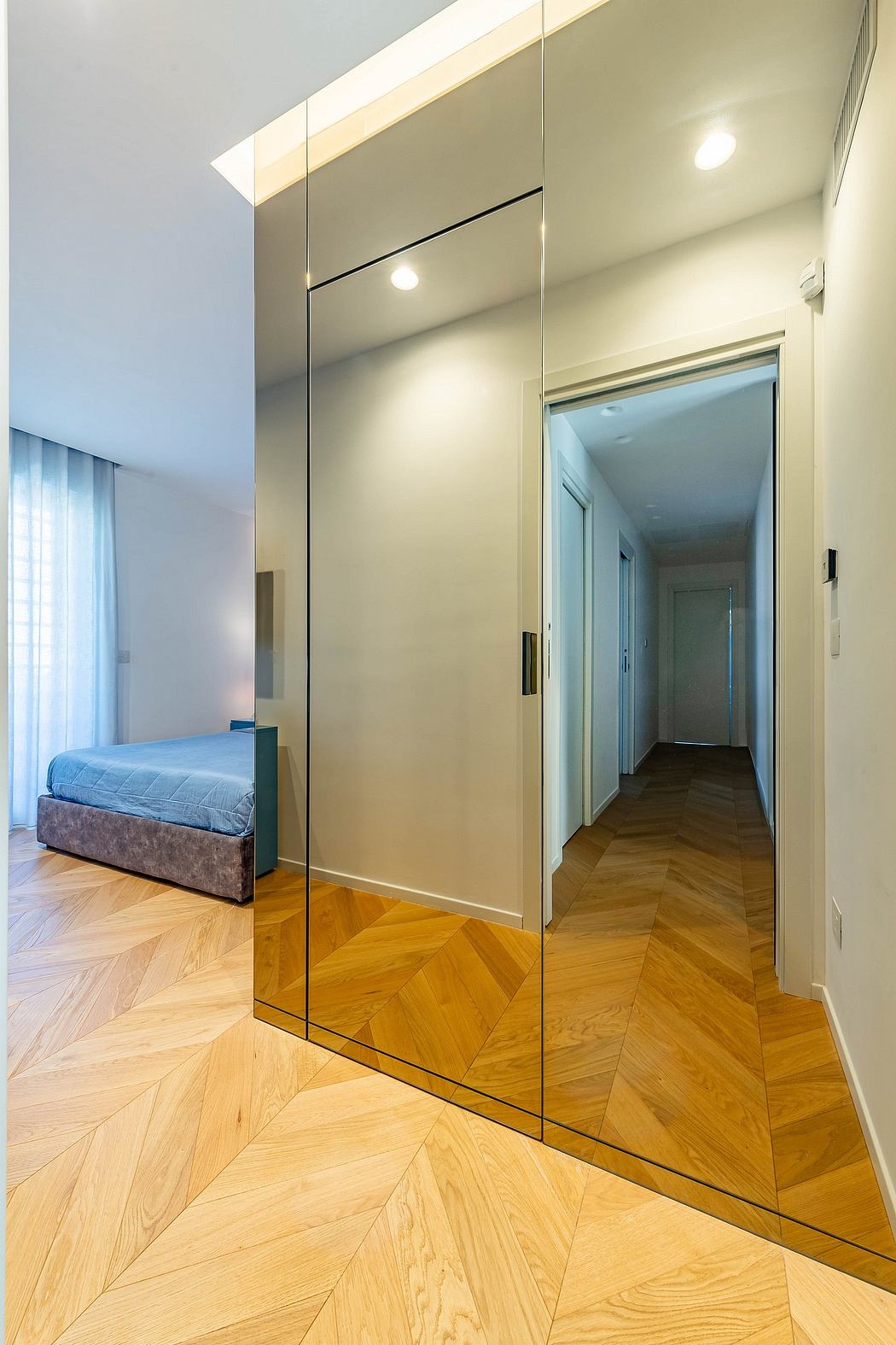 Elegant bedroom with floor-to-ceiling mirrored wardrobe, hardwood herringbone flooring.