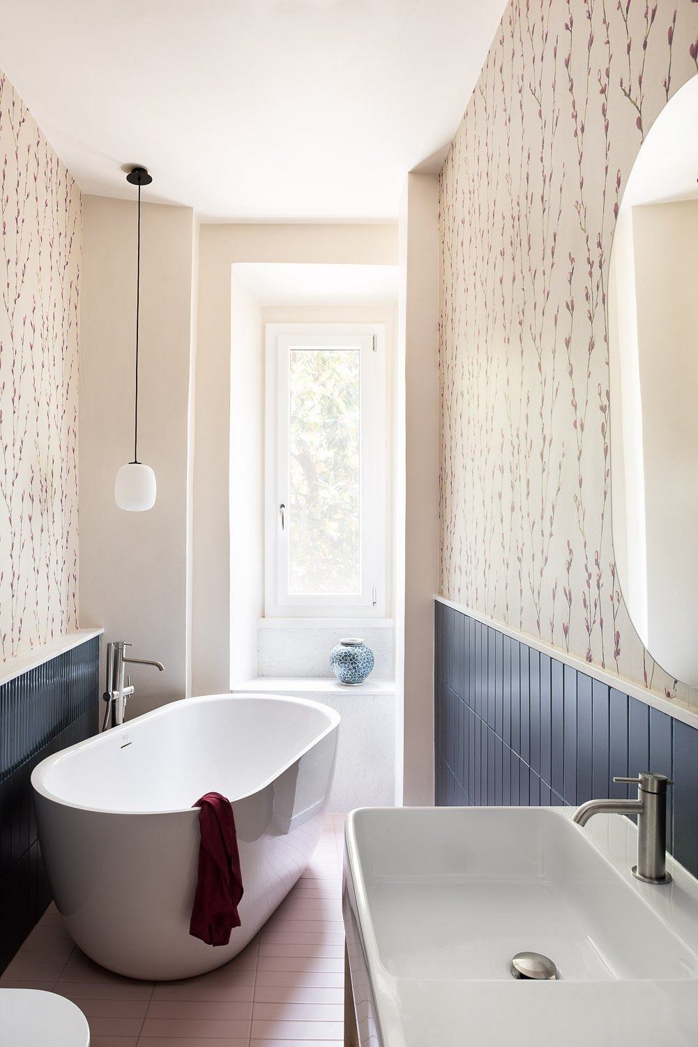 A modern bathroom with a freestanding bathtub, patterned wallpaper, and a sleek vanity.