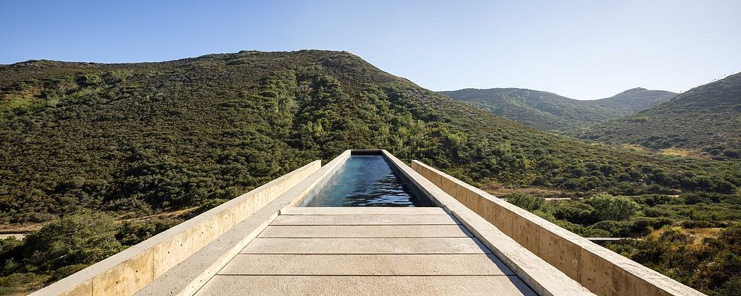 Wooden walkway leads to a rectangular pool with a mountainous, wooded backdrop.