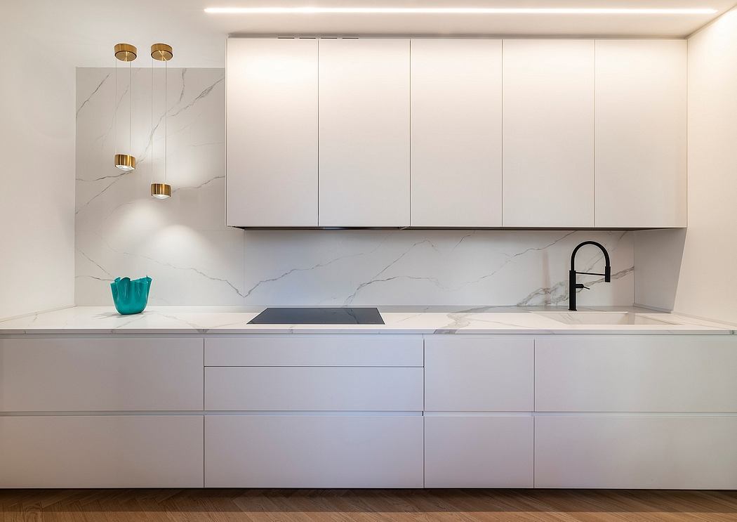 Sleek, minimalist kitchen with white cabinets, marble backsplash, and brass lighting fixtures.