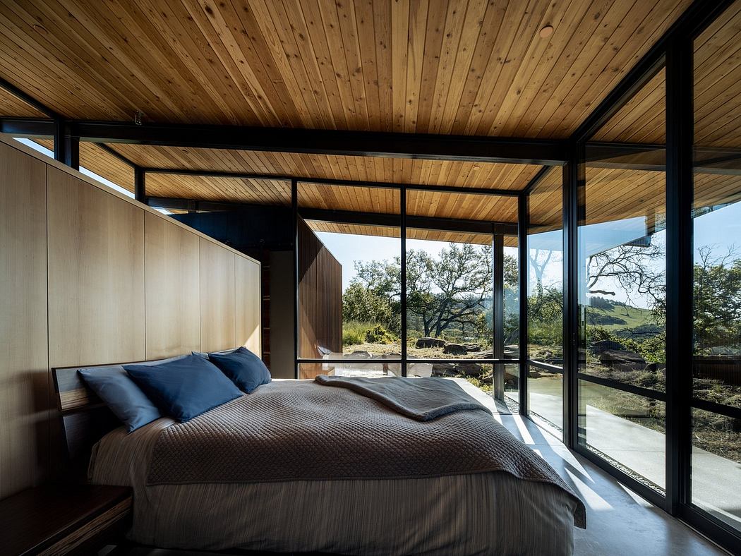Cozy cabin bedroom with expansive windows overlooking verdant landscape.