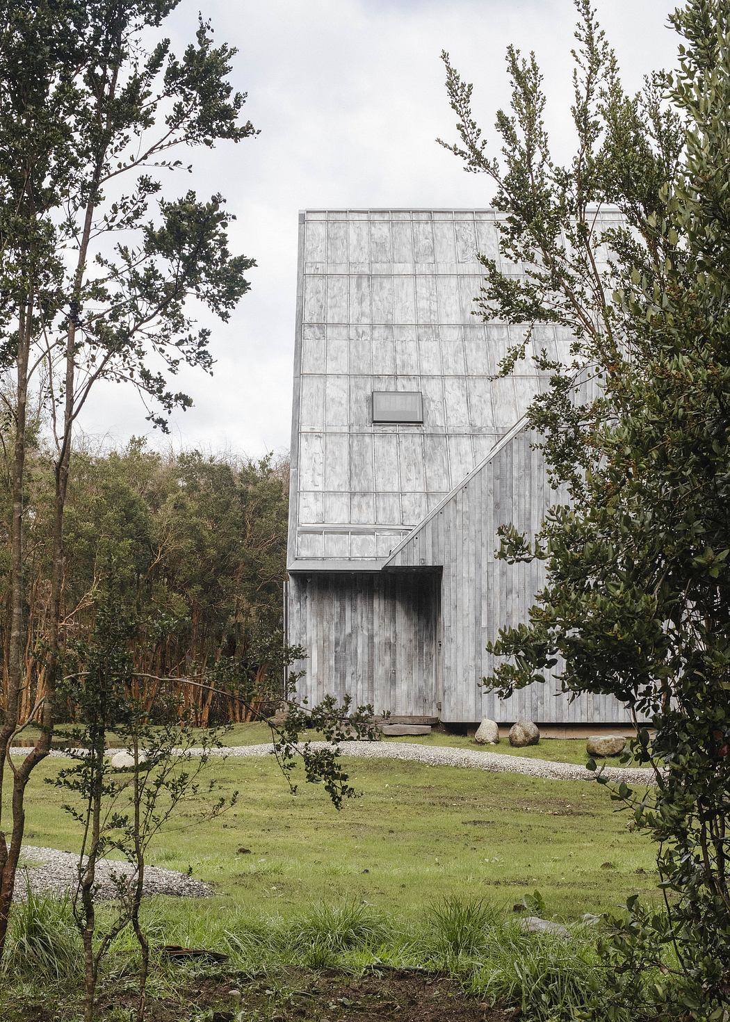 A modern, angular wooden structure nestled among lush greenery, with a grassy foreground.