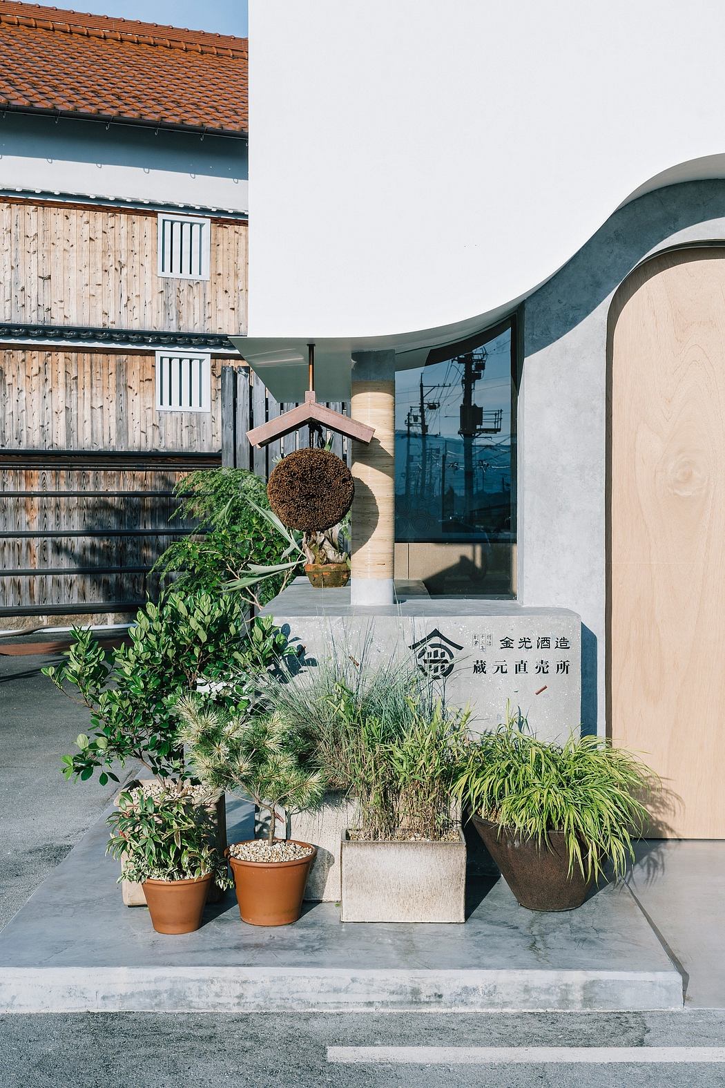 A modern architectural entrance with a curved canopy, wooden building, and various potted plants.