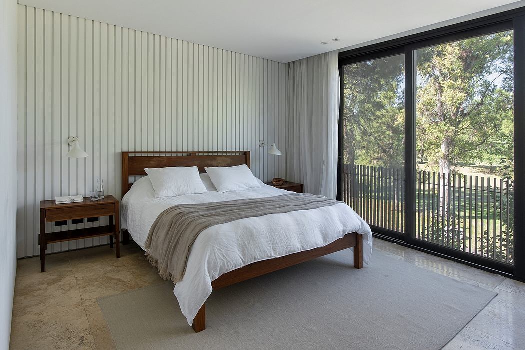 Modern bedroom with wooden bed frame, floor-to-ceiling windows, and nature view.