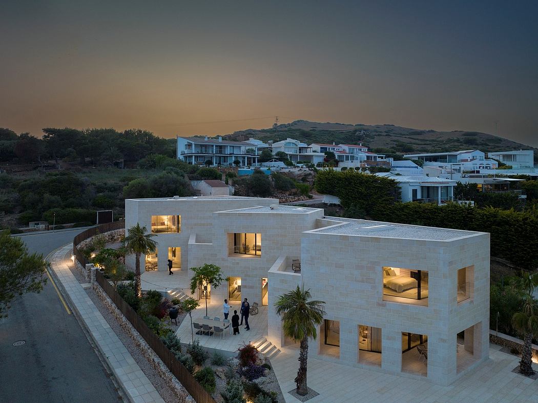 Modern architectural complex with illuminated cuboid structures, lush landscaping, and scenic mountain backdrop.