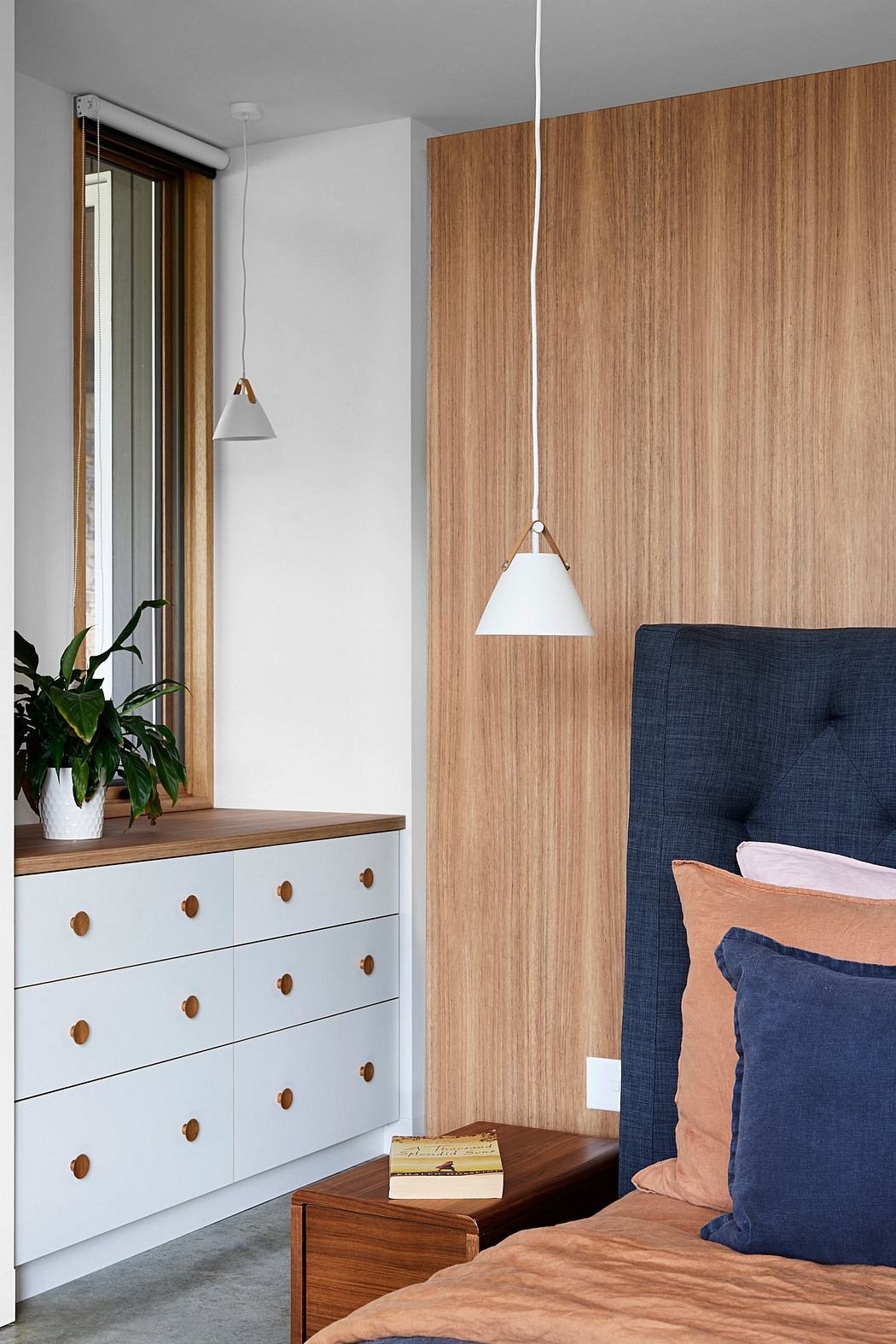 A modern bedroom with a wooden accent wall, white dresser, and pendant lamps.