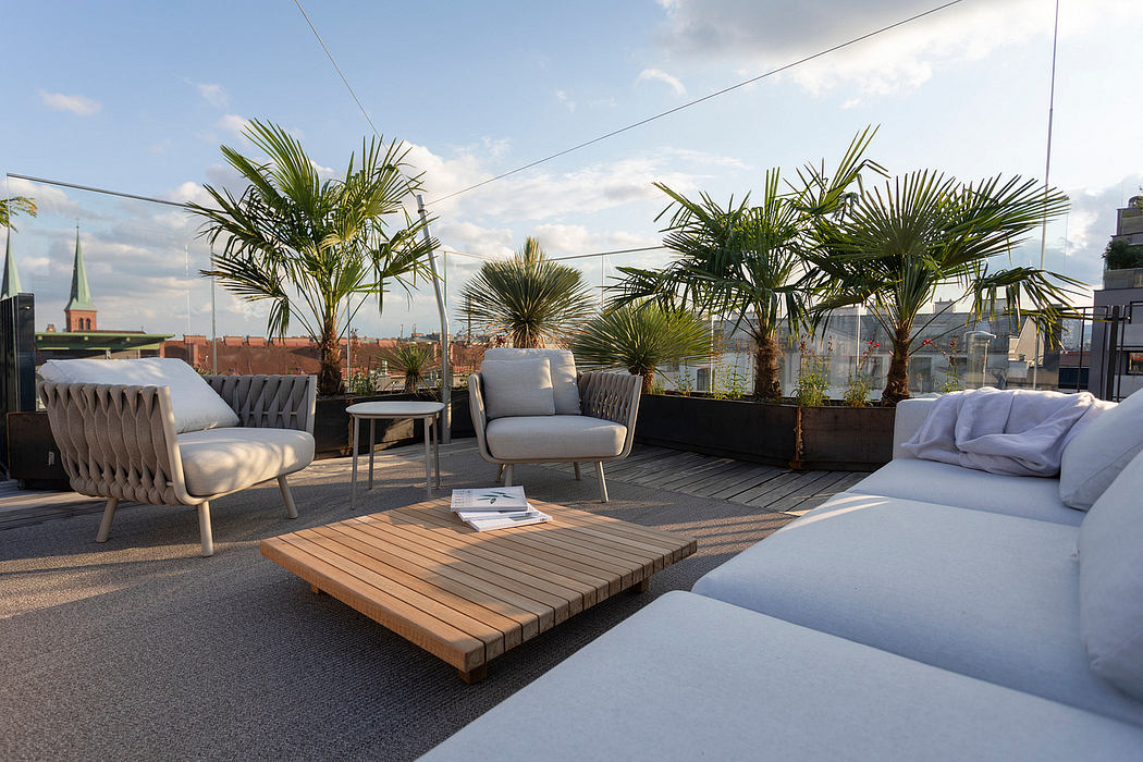 Rooftop oasis with plush seating, wood deck, and lush palm trees against city skyline.