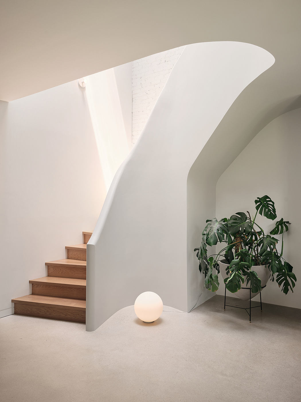 Modern staircase with curved wall, white globe lamp, and potted plant in minimalist interior.