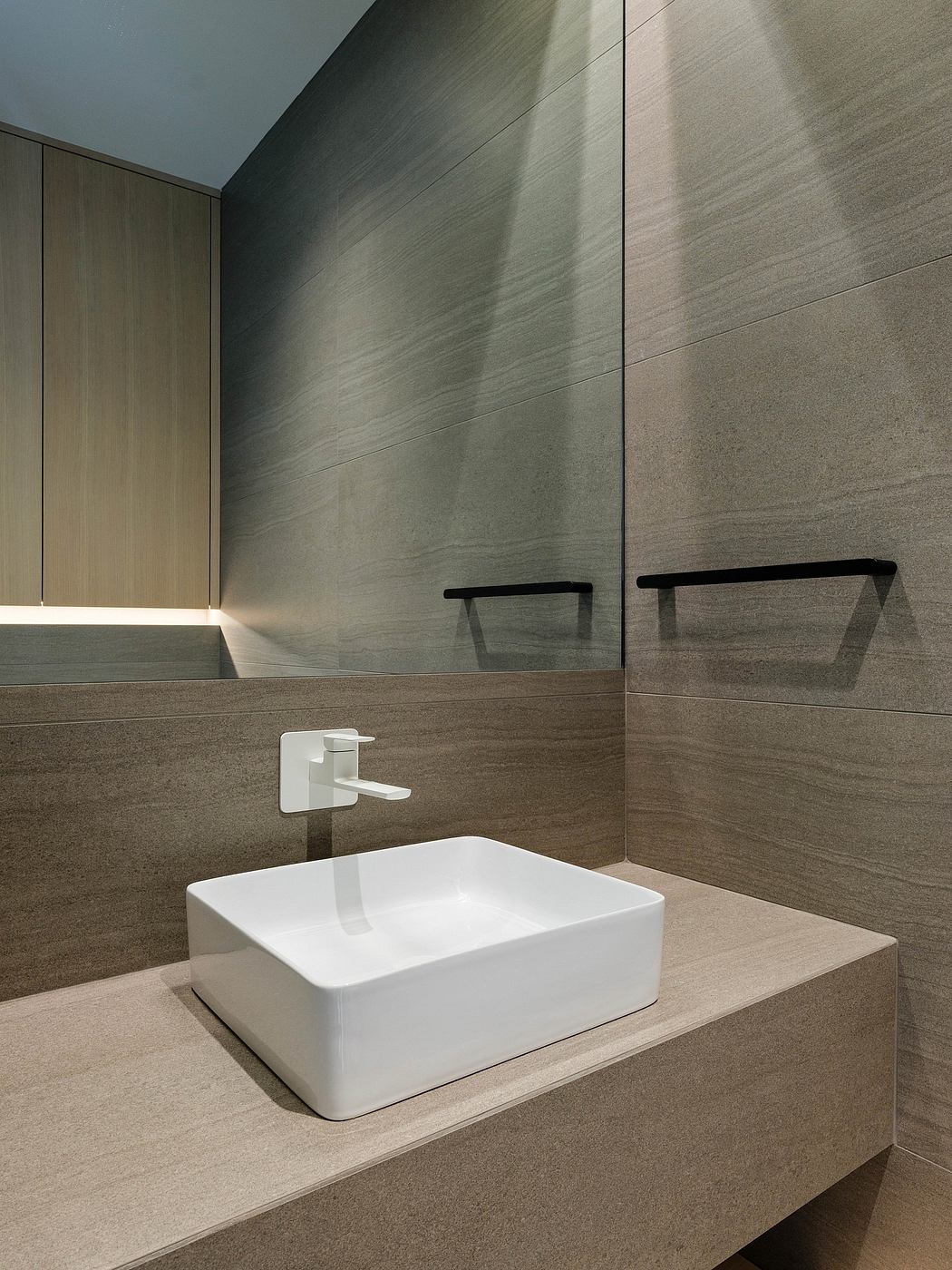 Modern, minimalist bathroom design with sleek white vessel sink, dark stone walls, and recessed lighting.