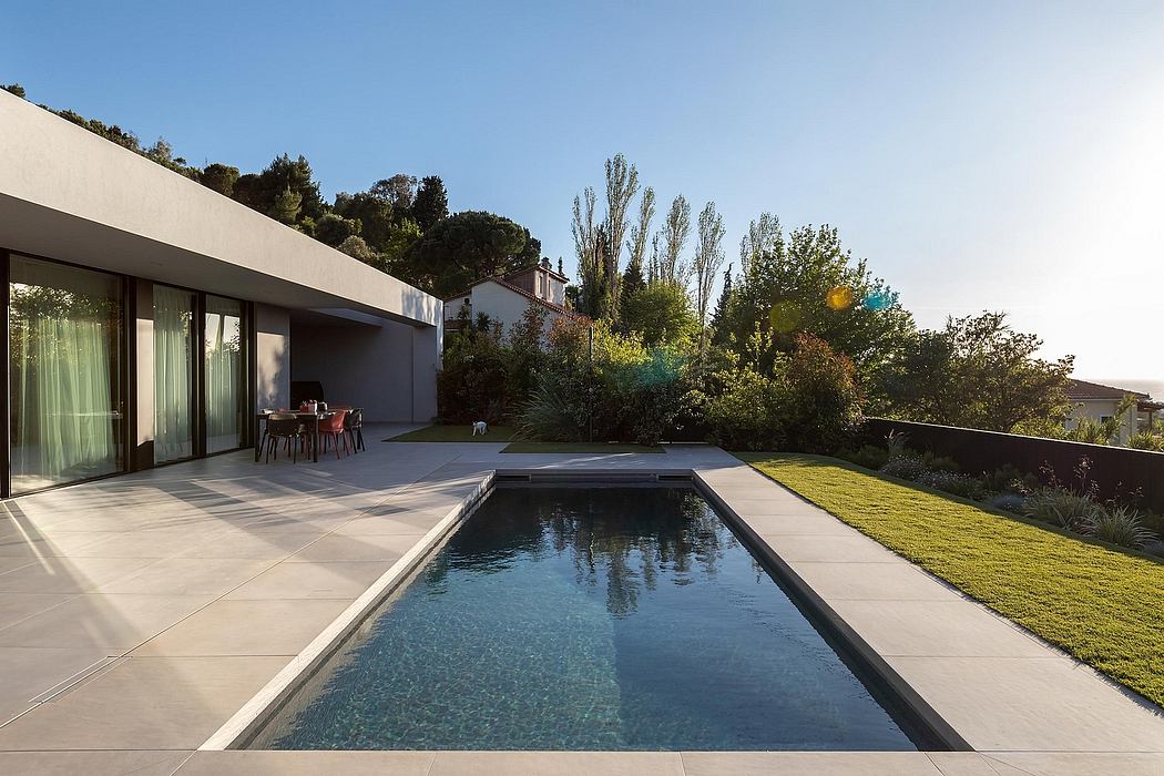 Modern home with clean lines, large glass doors, and a rectangular pool surrounded by lush greenery.