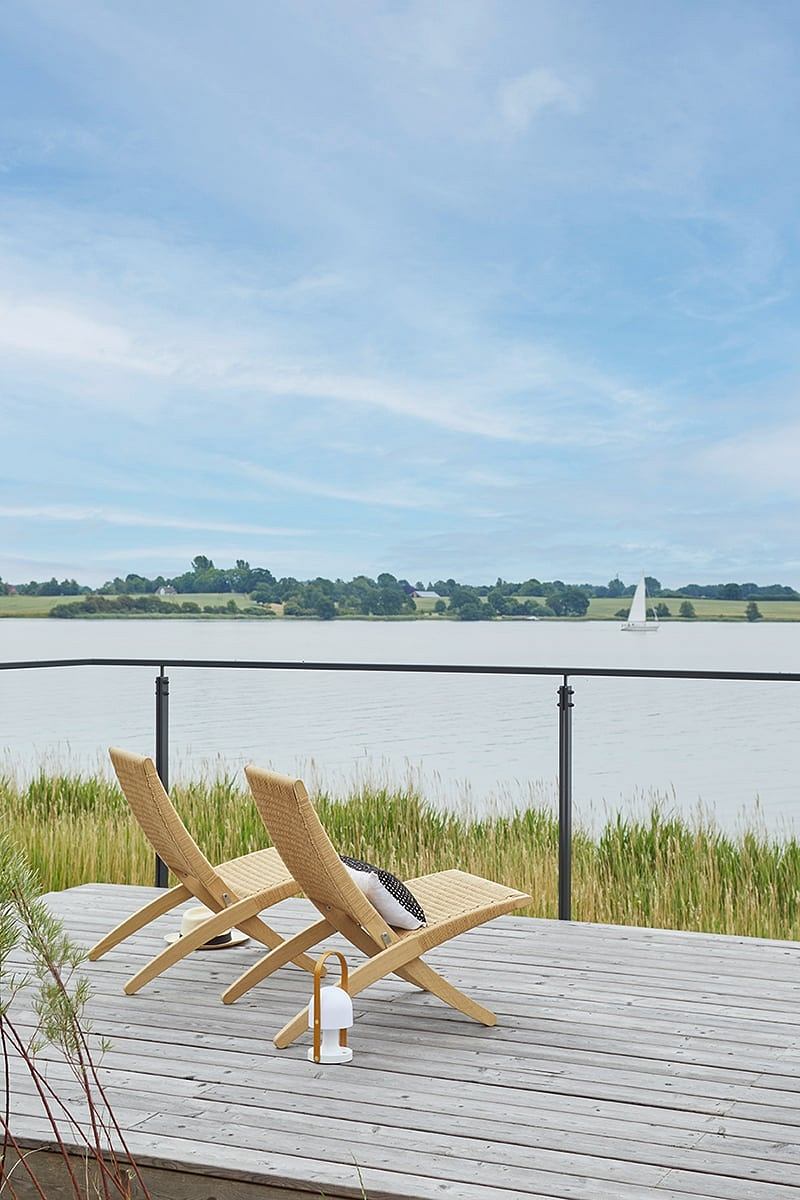 Relaxing lakefront deck with two woven chaise lounges and a tranquil water view.