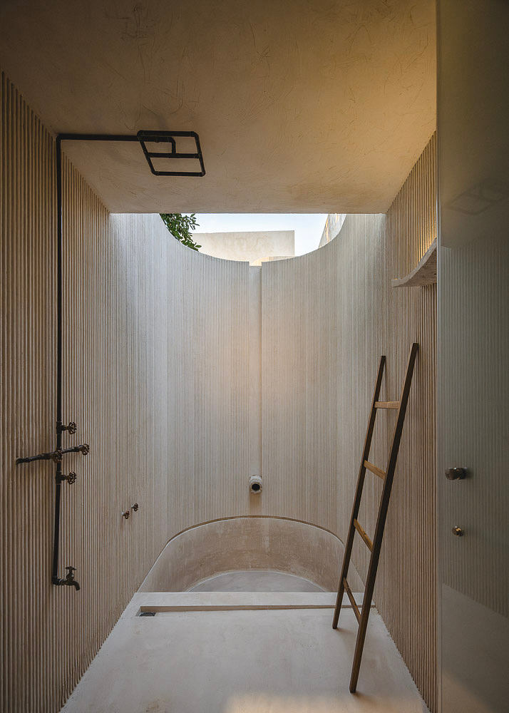 Minimalist bathroom interior with concrete bathtub, wood paneling, and ladder accent.