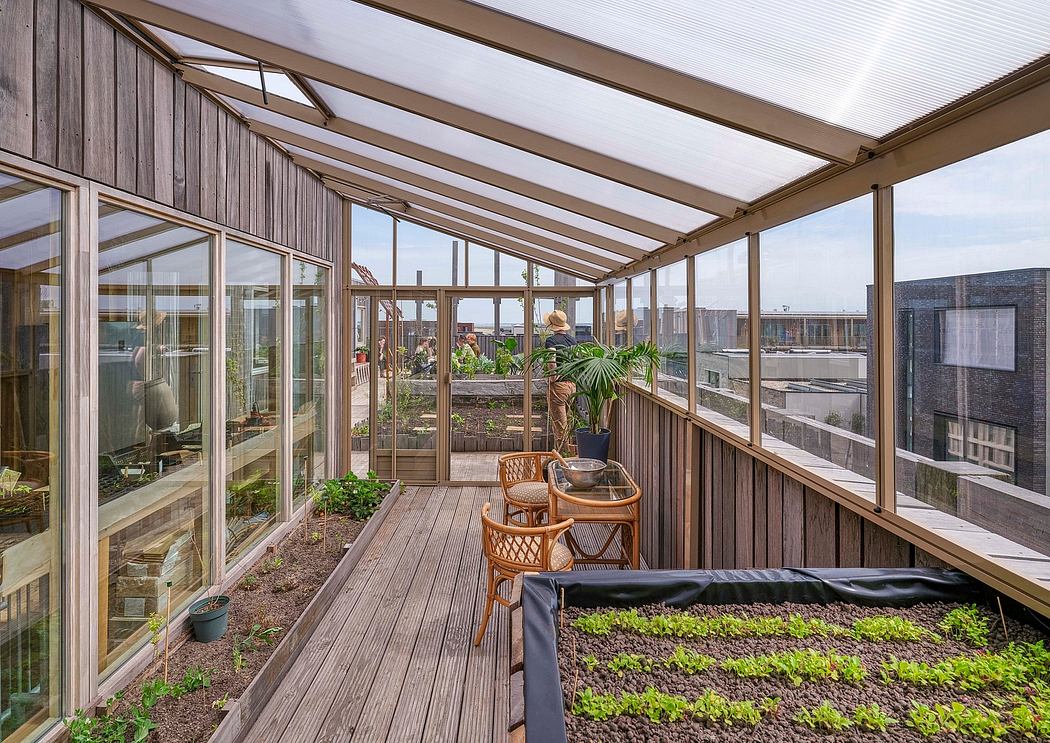 Wooden greenhouse with glass walls, plant boxes, and patio furniture on a wooden deck.
