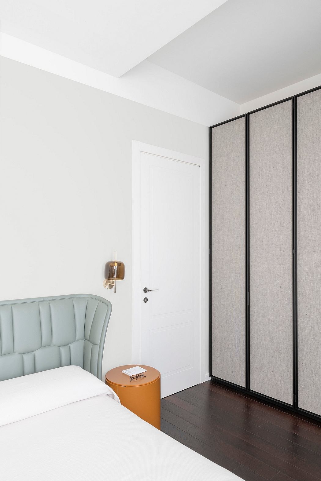 Minimalist bedroom with sleek black wardrobe, modern mint-green chair, and wooden side table.