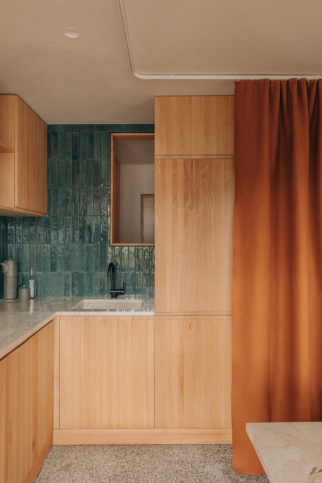 A kitchen with warm wood tones, a sleek tile backsplash, and rich orange curtains.