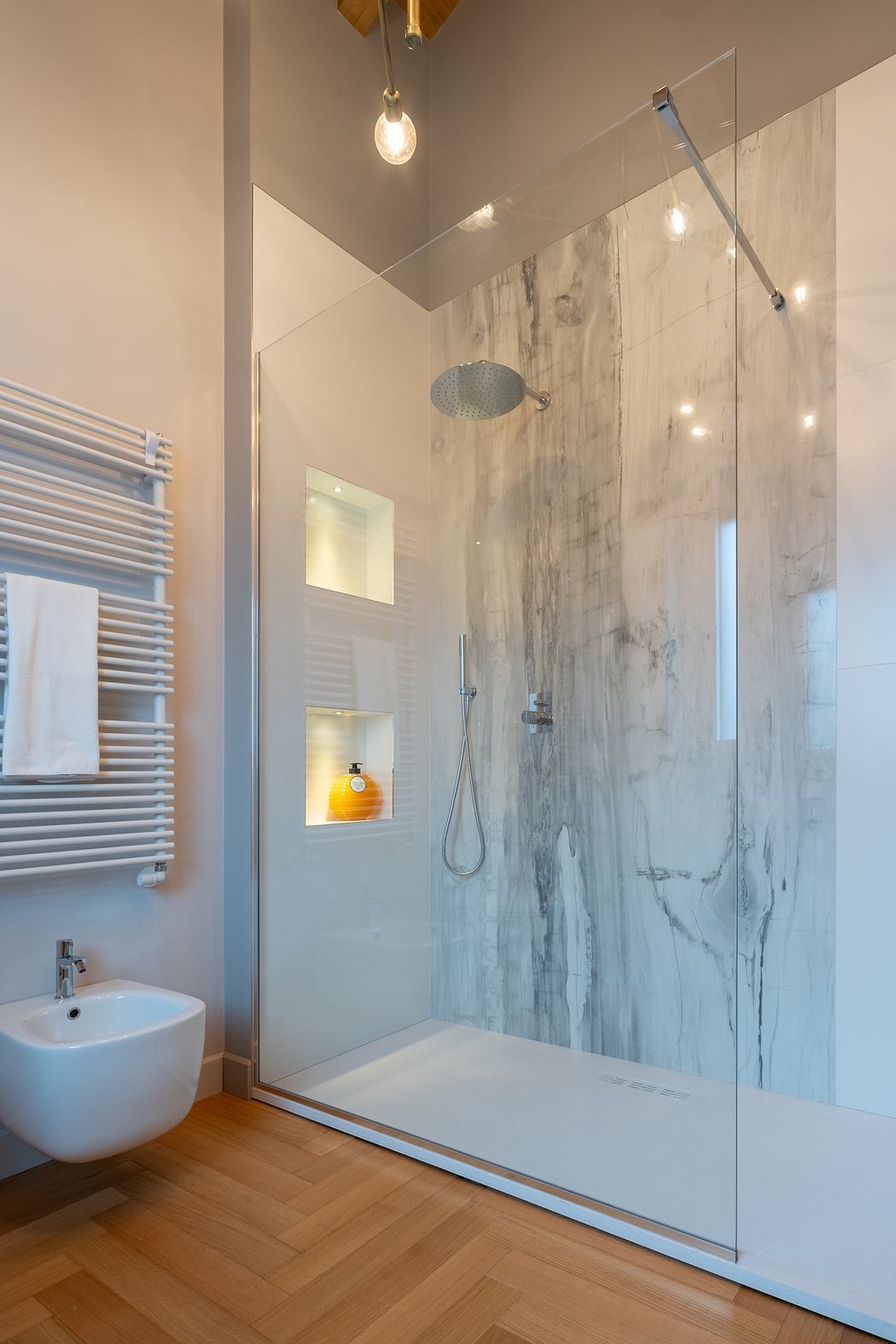 Sleek bathroom design with marble-patterned walls, glass shower enclosure, and wooden flooring.