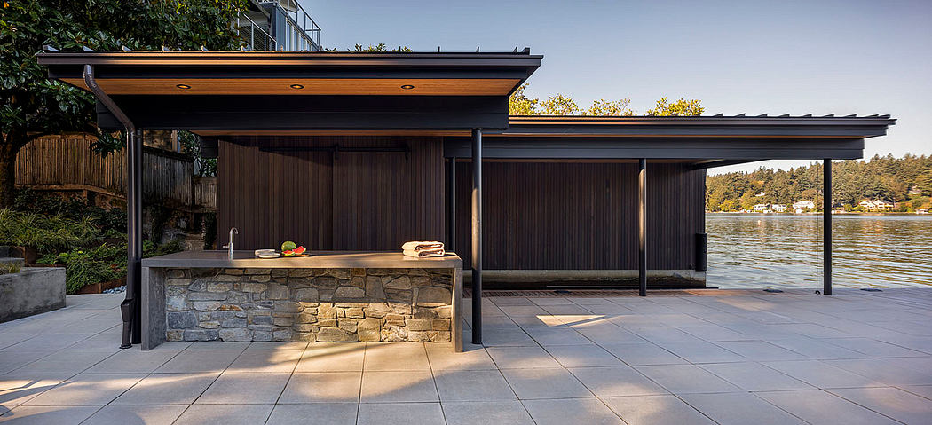 Sleek modern outdoor kitchen with stone veneer, timber beams, and scenic lake view.