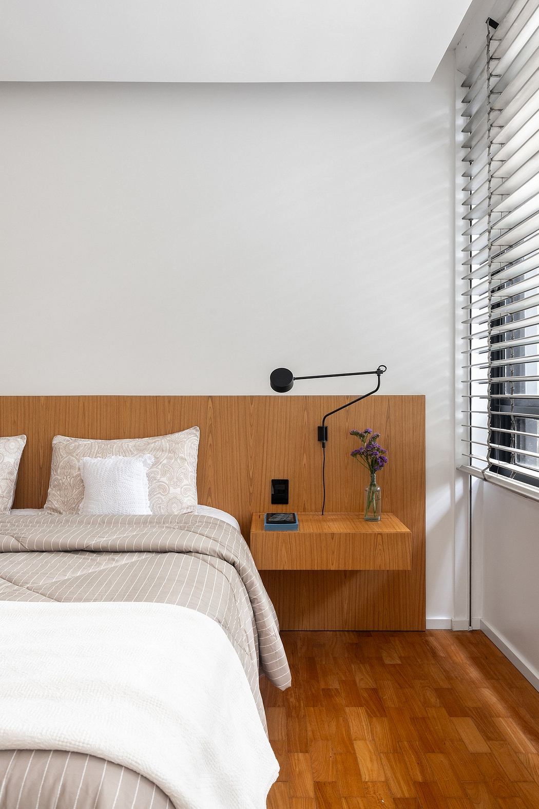 Minimalist bedroom with wooden headboard, nightstand, and adjustable lighting fixture.