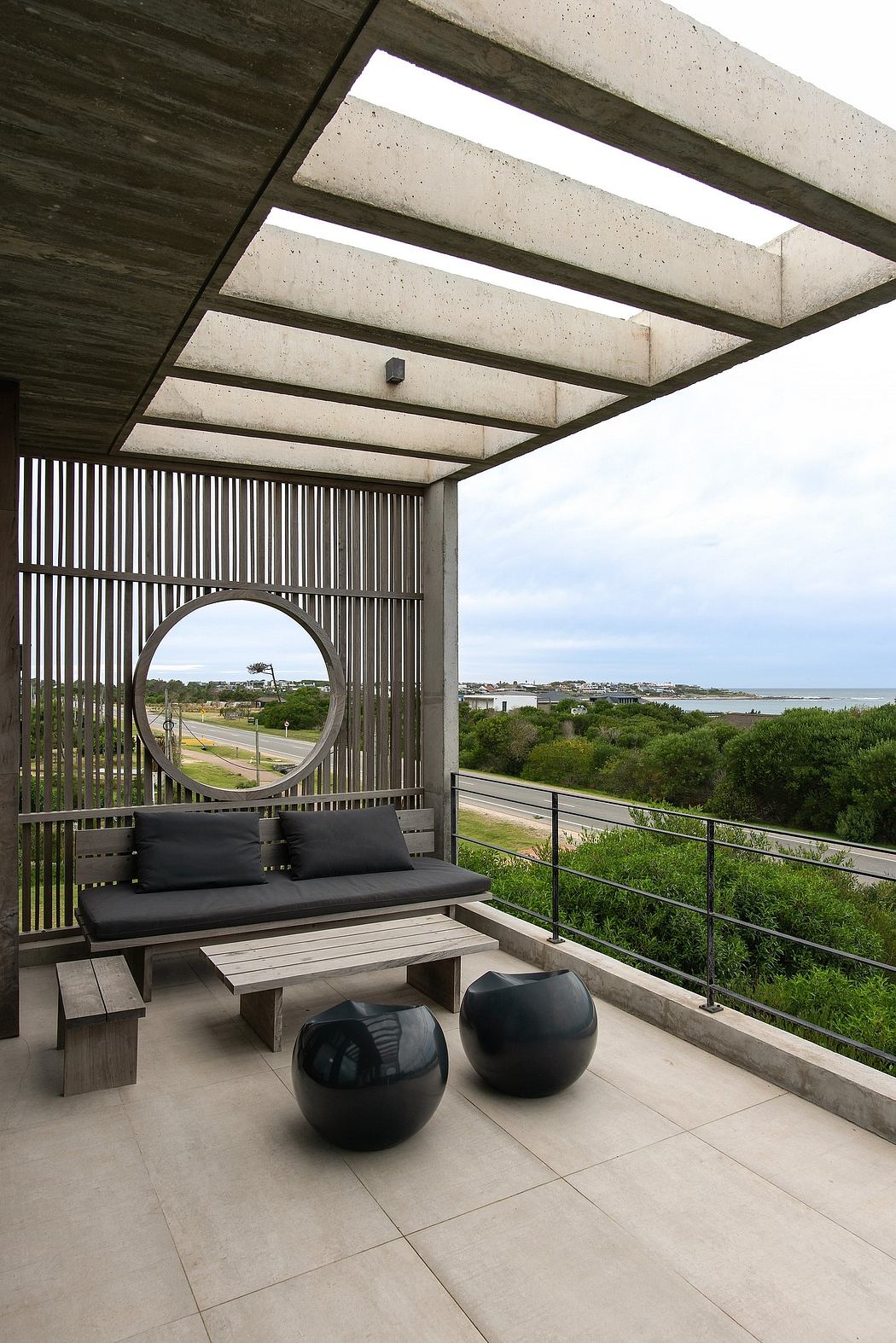 A modern concrete patio with sleek black furniture, circular mirror, and scenic view.