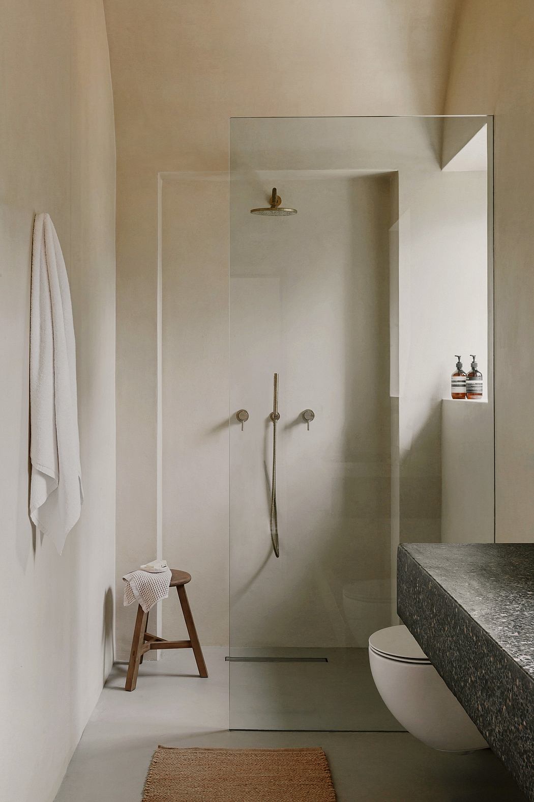 A minimalist bathroom with a stone vanity, glass shower enclosure, and wooden accents.