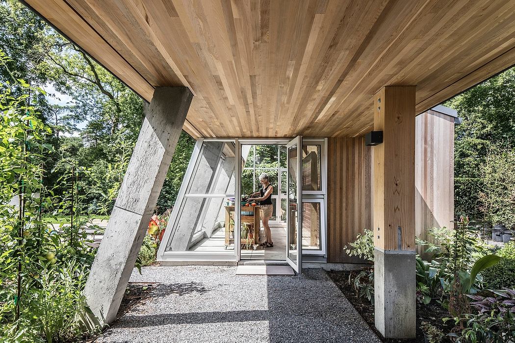 A rustic, wooden-clad structure with expansive windows and a gravel pathway leading to it, surrounded by lush greenery.