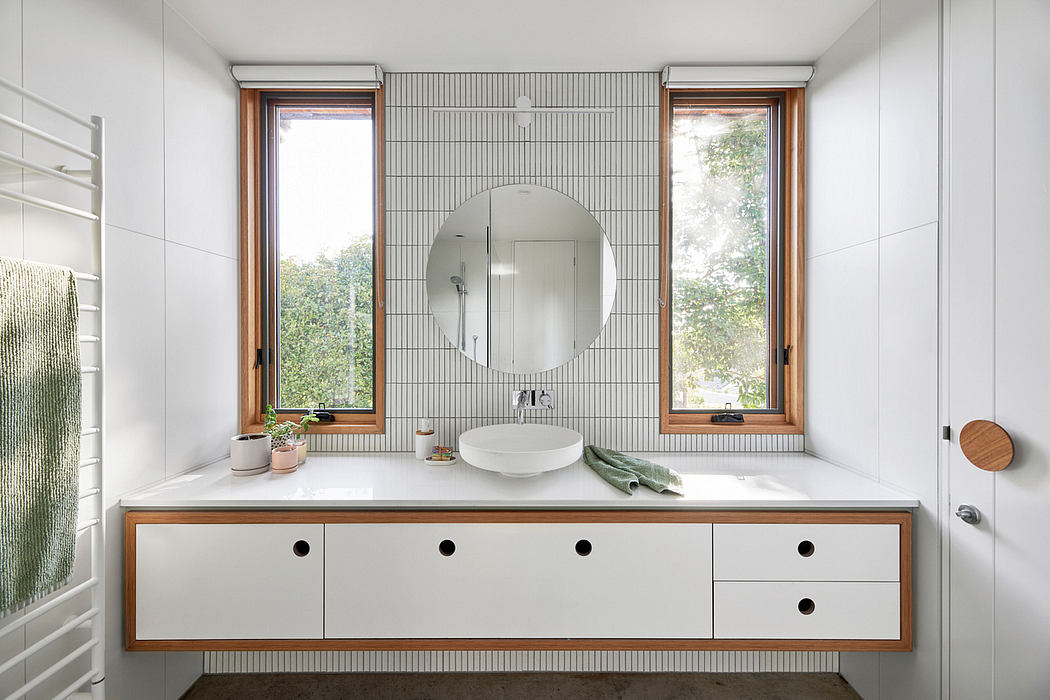 Modern bathroom with minimalist vanity, round mirror, and large windows overlooking nature.