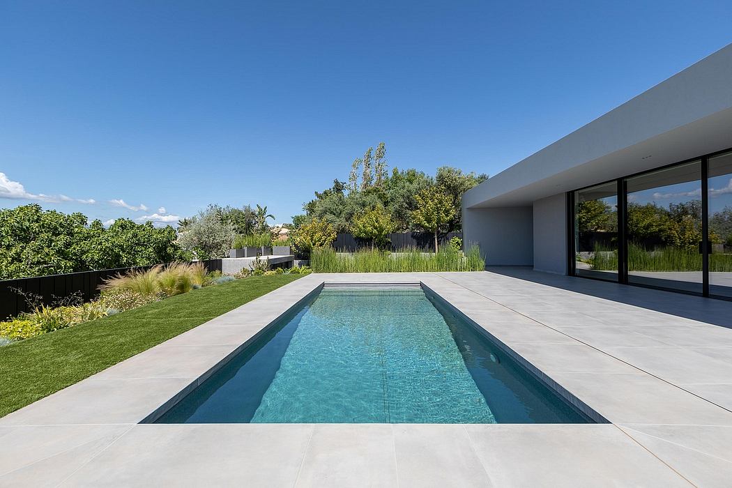 Sleek, modern house with minimalist architecture, expansive windows, and an infinity pool surrounded by lush greenery.