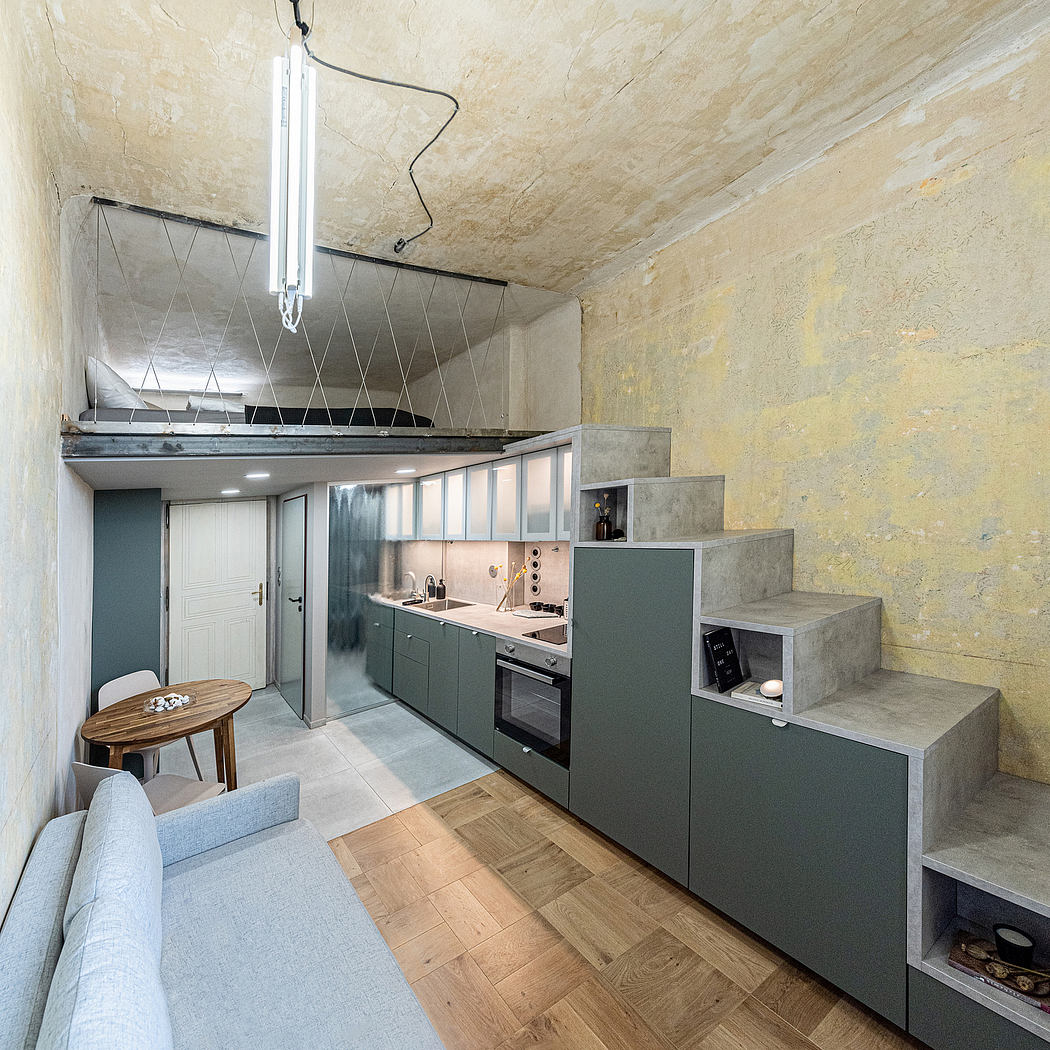 Small modern kitchenette in a compact studio apartment with concrete walls, wooden floors, and built-in storage.