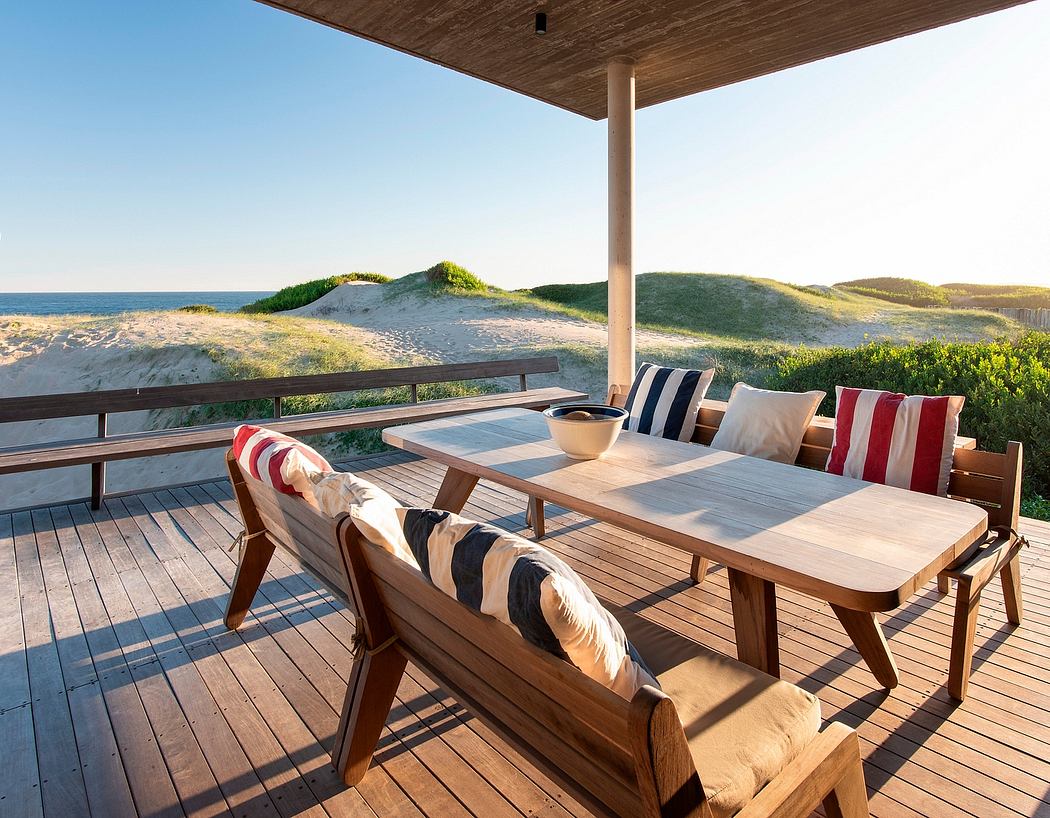 Cozy coastal patio with wooden furniture, striped pillows, and a view of sand dunes.