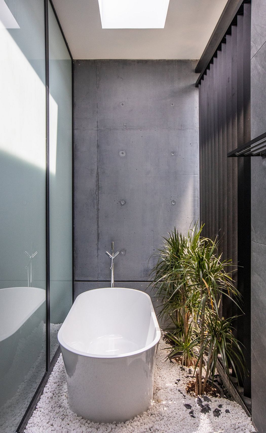 Sleek, minimalist bathroom with freestanding tub, concrete wall, and lush plant features.