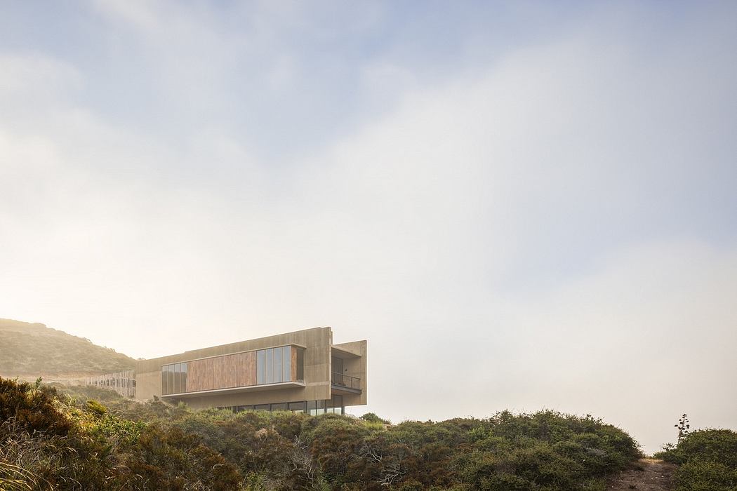 A modern, multi-story residential structure with extensive glass and wood paneling, situated in a lush, hilly landscape.