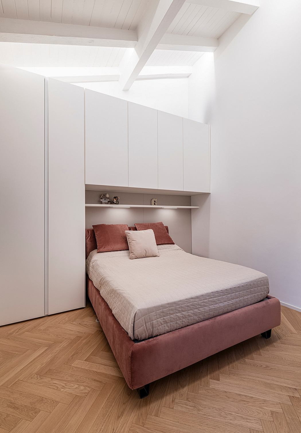 A modern, minimalist bedroom with clean white walls, built-in cabinets, and a burgundy upholstered bed frame.