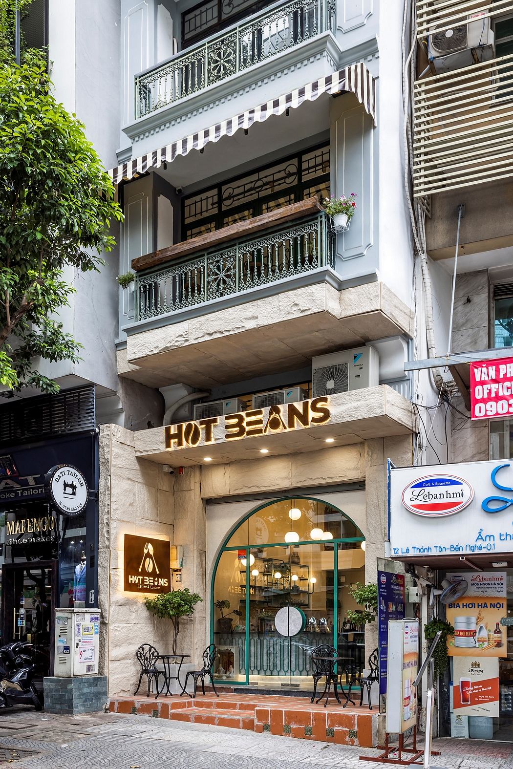 Ornate wrought-iron balconies, stone facade, and neon sign of a Vietnamese restaurant.