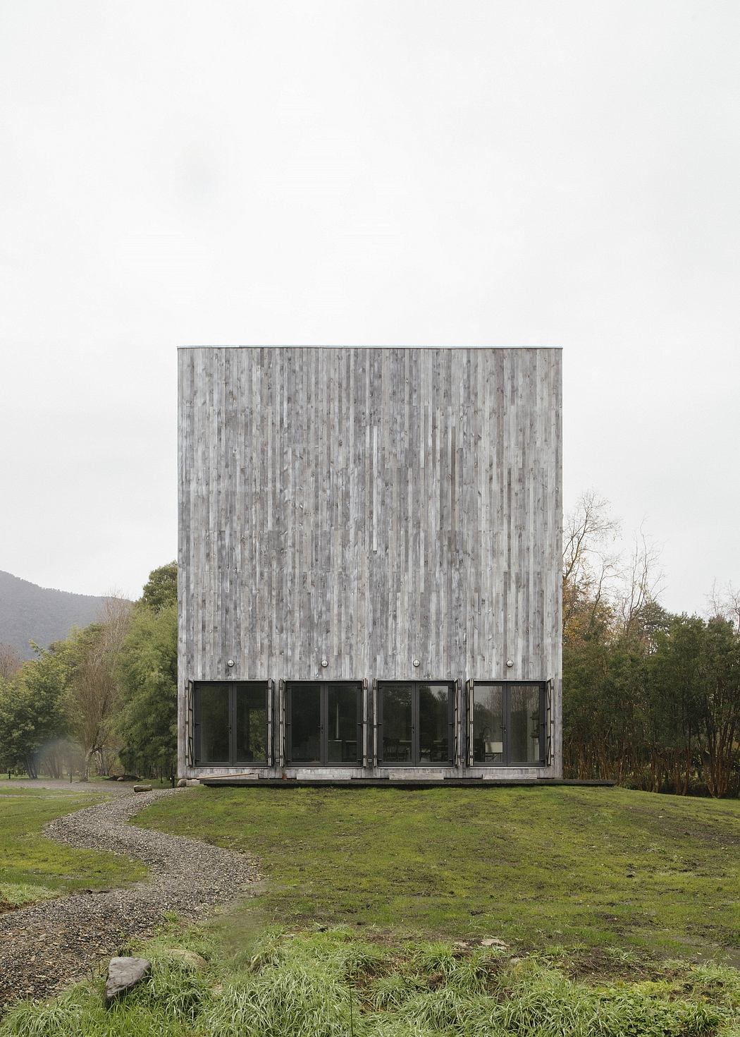 A minimalist, wooden structure with large windows and a lush, green meadow.