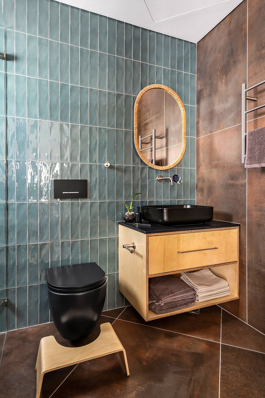 Sleek bathroom with teal tile wall, wooden vanity, black vessel sink, and oval mirror.