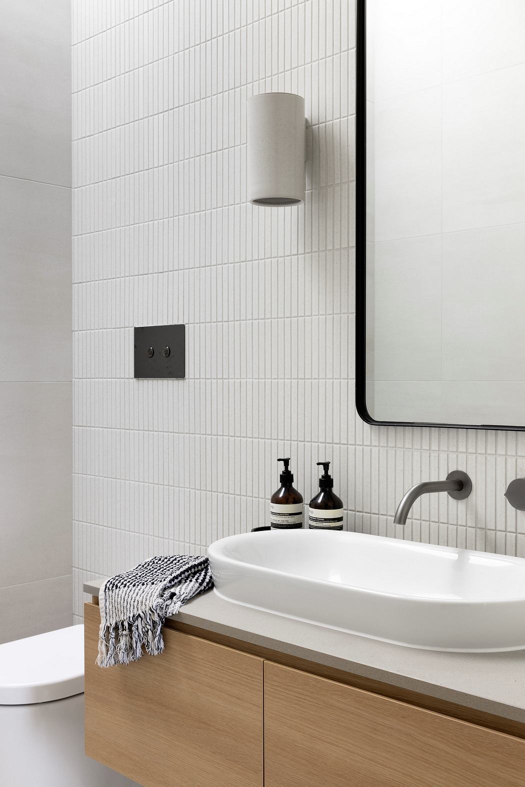 A modern bathroom with a white tile wall, a round wash basin, and a wooden vanity unit.