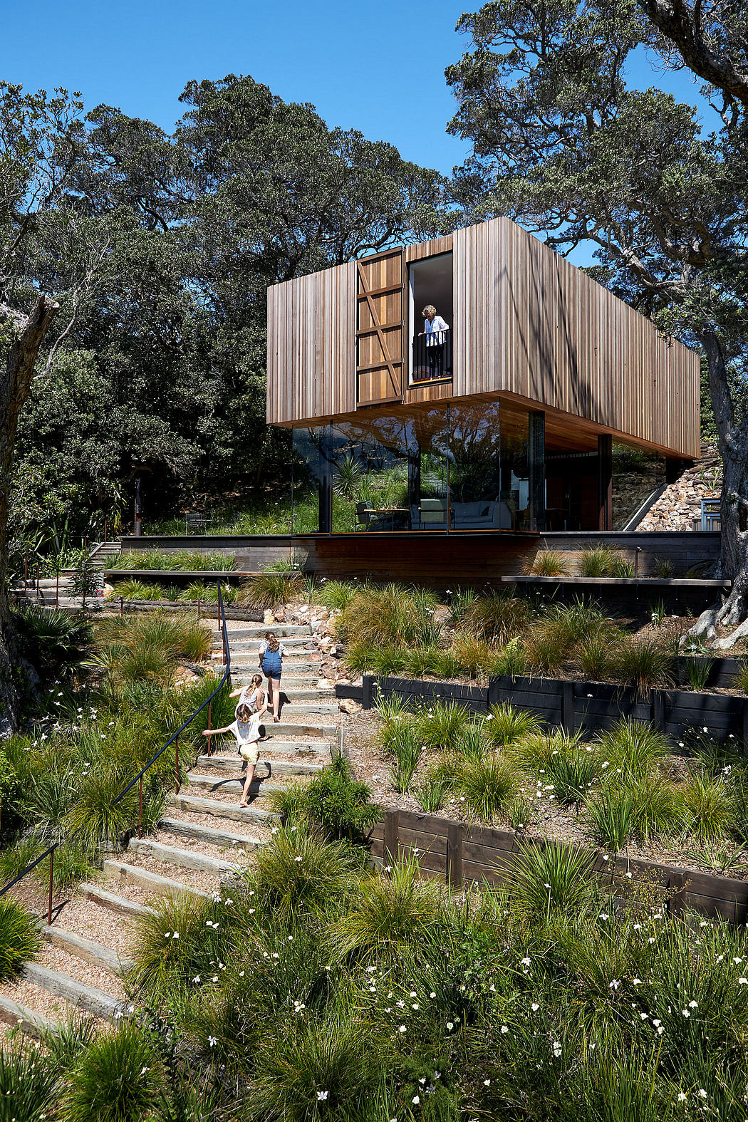 A modern, elevated wooden cabin nestled among lush trees and a winding stone staircase.